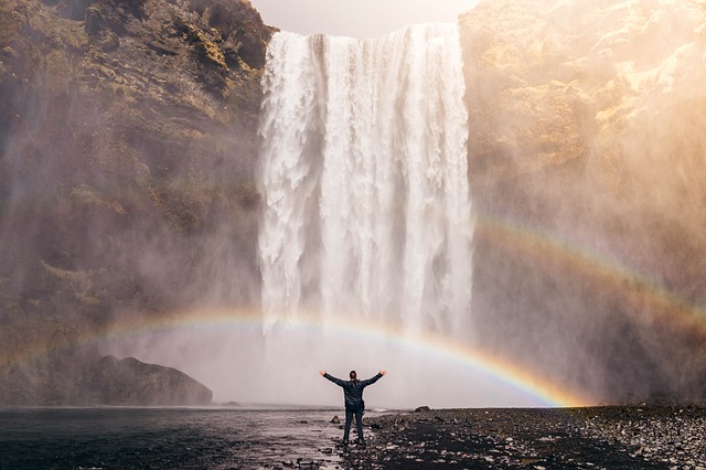man with extended arms in front of waterfall